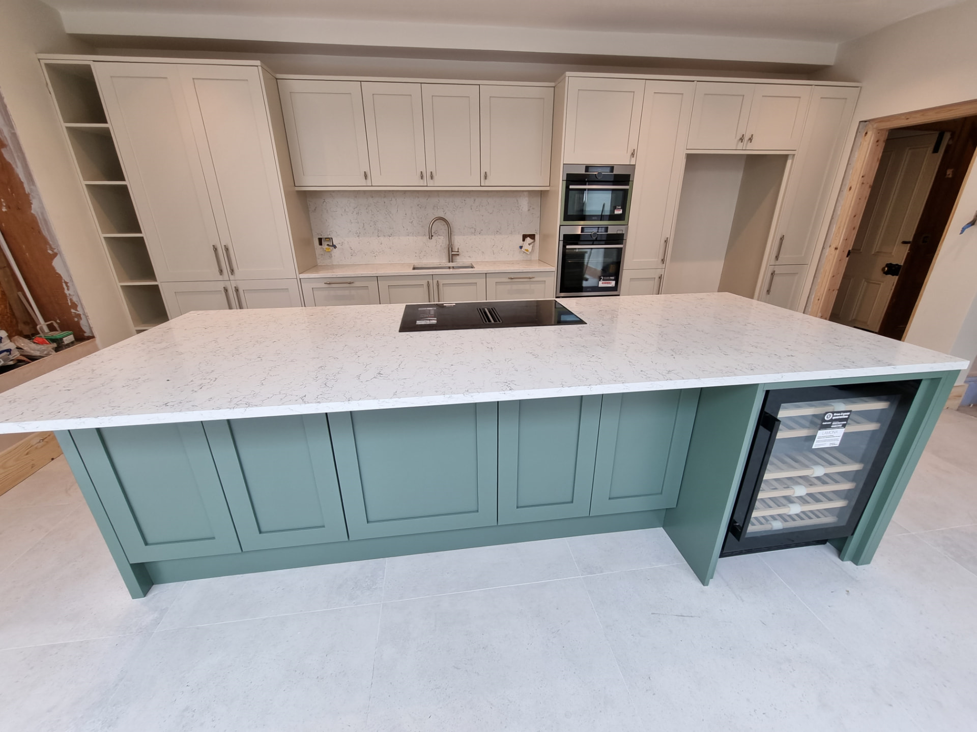 A finished two-tone kitchen with sage green island, light worktops and cream shaker cabinets